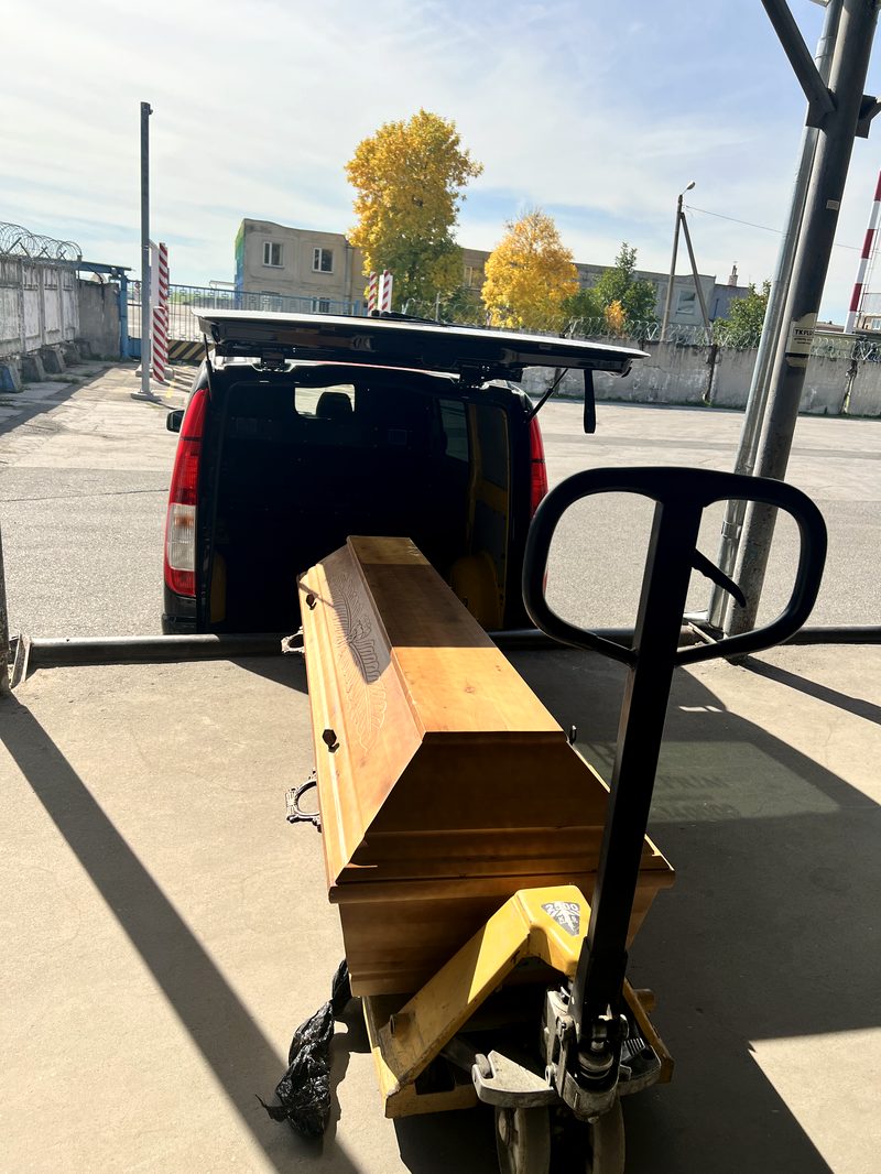 Завантаження труни на візку до ритуального мікроавтобуса перед рейсом в Україну