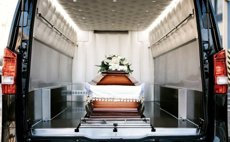 Труна з квітами всередині ритуального автомобіля з відчиненими дверима