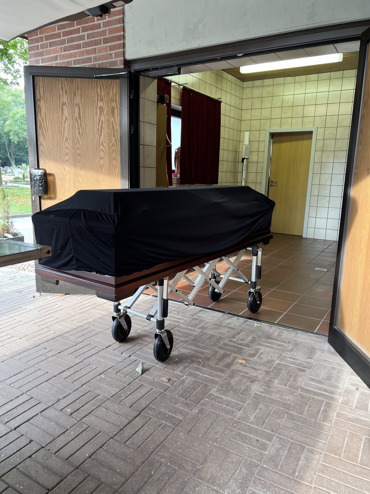 Sarg unter einer schwarzen Decke auf einem Wagen am Eingang eines Gebäudes