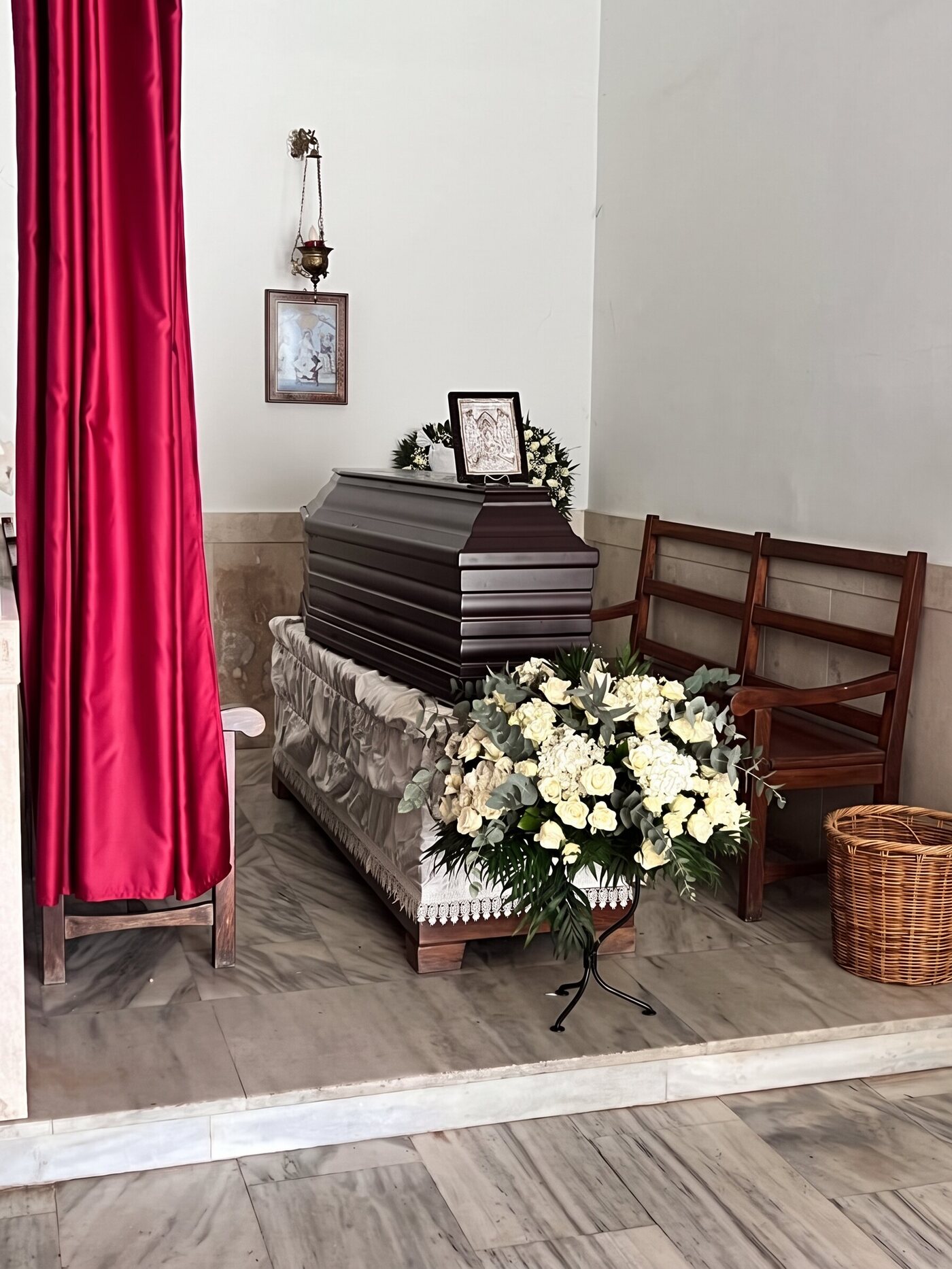 Geschlossener dunkler Sarg in einer Kapelle mit einer Ikone, weißen Blumen und einem roten Vorhang