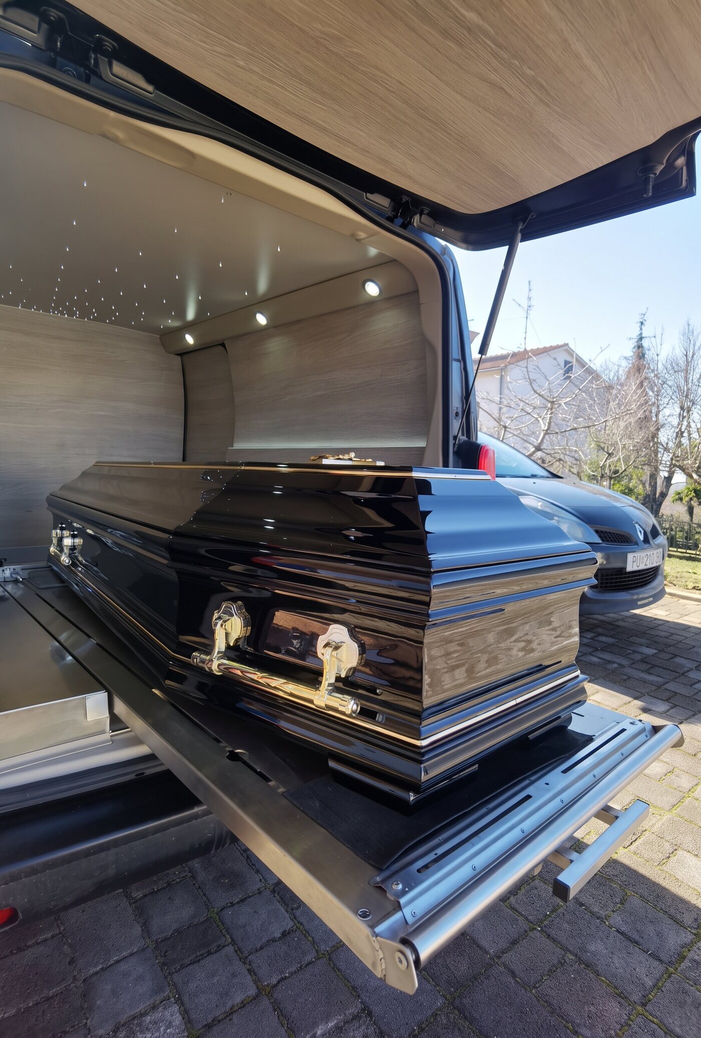 Schwarz lackierter Sarg auf dem ausfahrbaren Boden eines Bestattungswagens