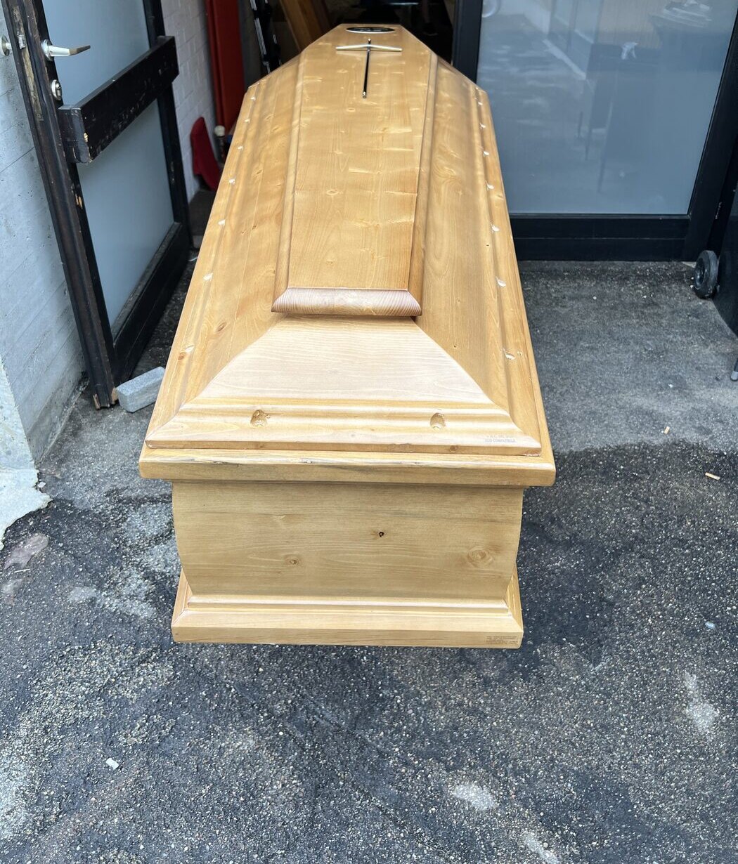 Kiefernsarg mit einem Kreuz neben Glastüren